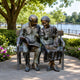 Life-Size Traditional Elderly Couple on Bench Bronze Sculpture (Book and Cat) - 170cm, shown outdoors on a park path with greenery and a lake in the background.