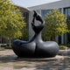 Monumental Modern Abstract Mother and Infant Bronze Sculpture, 300cm, black biomorphic base with two figures reaching upward, displayed outdoors on a round stone plinth near trees and a glass building.