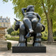 Monumental Rotund Nude Figure and Donkey Bronze Sculpture, 300cm, black cast bronze figure reclining atop a donkey, displayed outdoors on a dark plinth near trees and a garden path.
