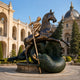 Monumental Classical Warrior on Rearing Horse and Dragon Bronze Sculpture, 320cm, gold-toned rider spearing a green dragon, displayed on a plaza platform before a palace facade.