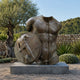 Large Contemporary Fragmentary Warrior Torso Bronze Sculpture, 200cm, headless male torso with relief shield on a stone base, set outdoors near a garden wall.