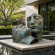 Monumental Contemporary Two Faces Bronze Sculpture, 180cm, two abstracted heads with green-brown patina leaning together on a stone plinth beside a reflecting pool.