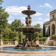Monumental Classical Tiered Fountain Bronze Fountain (Maidens and Cherubs), 700cm, with reclining draped maidens at the base and cherub figures above, set in a landscaped garden courtyard.