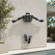 Contemporary Emerging Male Figure Bronze Wall Sculpture, 60cm, mounted on an exterior wall with torso and arms above and feet below, near a pool and greenery.