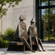 Large Modern Geometric Seated Figures Bronze Sculpture, 250cm, faceted bronze figures with block and pyramid heads seated on a bench outside a glass and concrete building.
