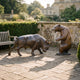 Monumental Traditional Charging Bull and Rearing Bear Bronze Sculpture Set by Giant Sculptures displayed on a stone terrace beside a wooden bench.