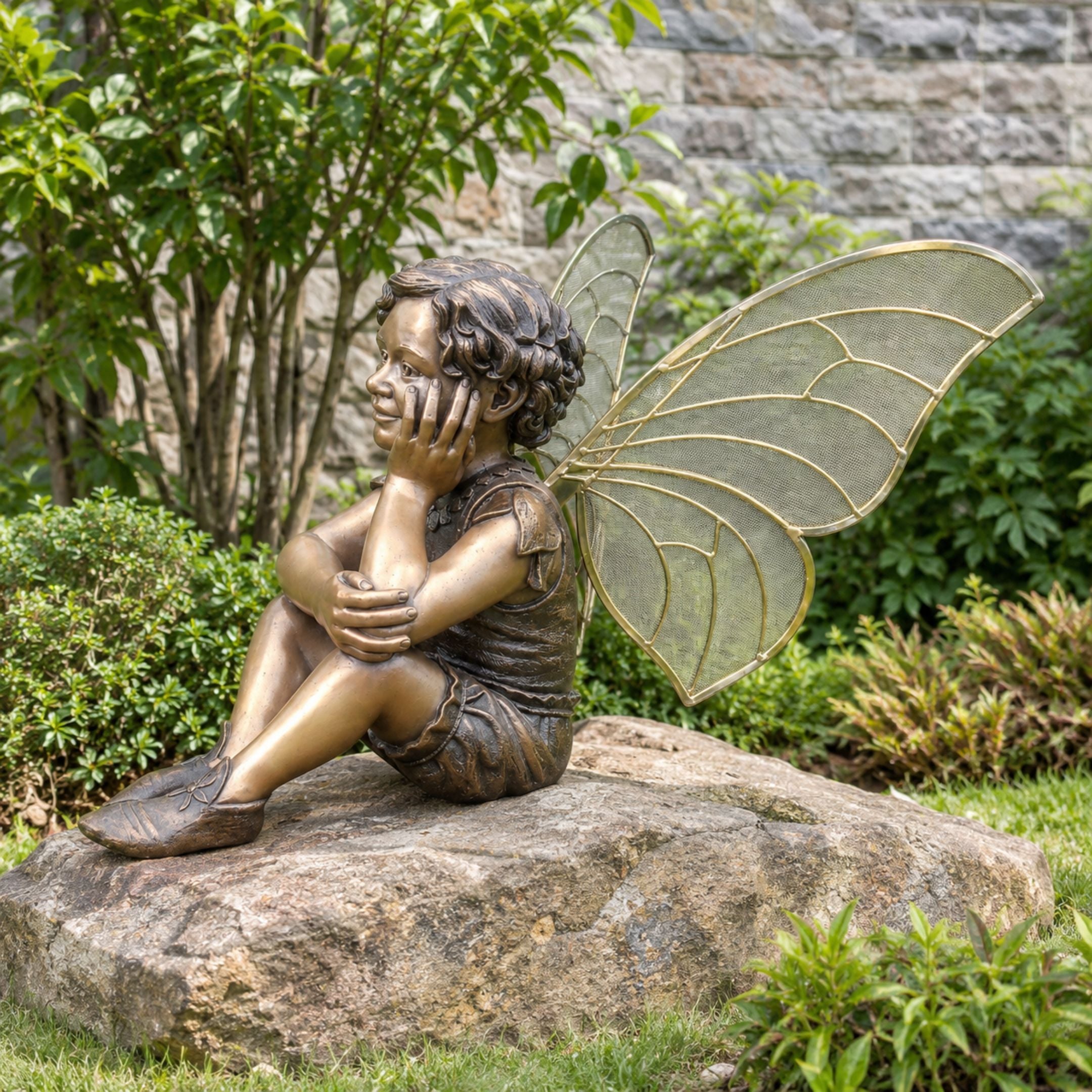 Traditional Fairy Boy Child Bronze Sculpture, 150cm, seated figure with hands to face and large golden-veined wings, set on a garden stone.