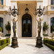 Monumental Classical Goddess Candelabra Bronze Sculpture Pair, 210cm, flanking a mansion entrance with bronze figures raising nine-arm candelabras above urn-shaped bases.