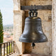 Large Traditional Inscribed Church Bell Bronze Sculpture, 120cm, dark bronze finish with "Saint Louis" lettering, mounted on a wooden beam in a stone bell tower overlooking a hillside town.