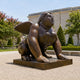 Monumental Contemporary Winged Female Sphinx Bronze Sculpture, 250cm, in a sphinx-like crawl with wings raised, outdoors on a stone base near trees.