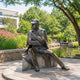 Large Traditional Seated Contemplative Figure Bronze Sculpture, 180cm, seated man in deerstalker cap and overcoat holding a pipe, set outdoors near a garden pond.