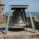 Large Traditional Bronze Bell Sculpture - 90cm, mounted in a four-legged A-frame stand outdoors near a stone wall overlooking water.