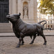 Life-Size Charging Bull Bronze Sculpture by Giant Sculptures shown in side profile on cobblestones before a classical stone building with a niche statue.