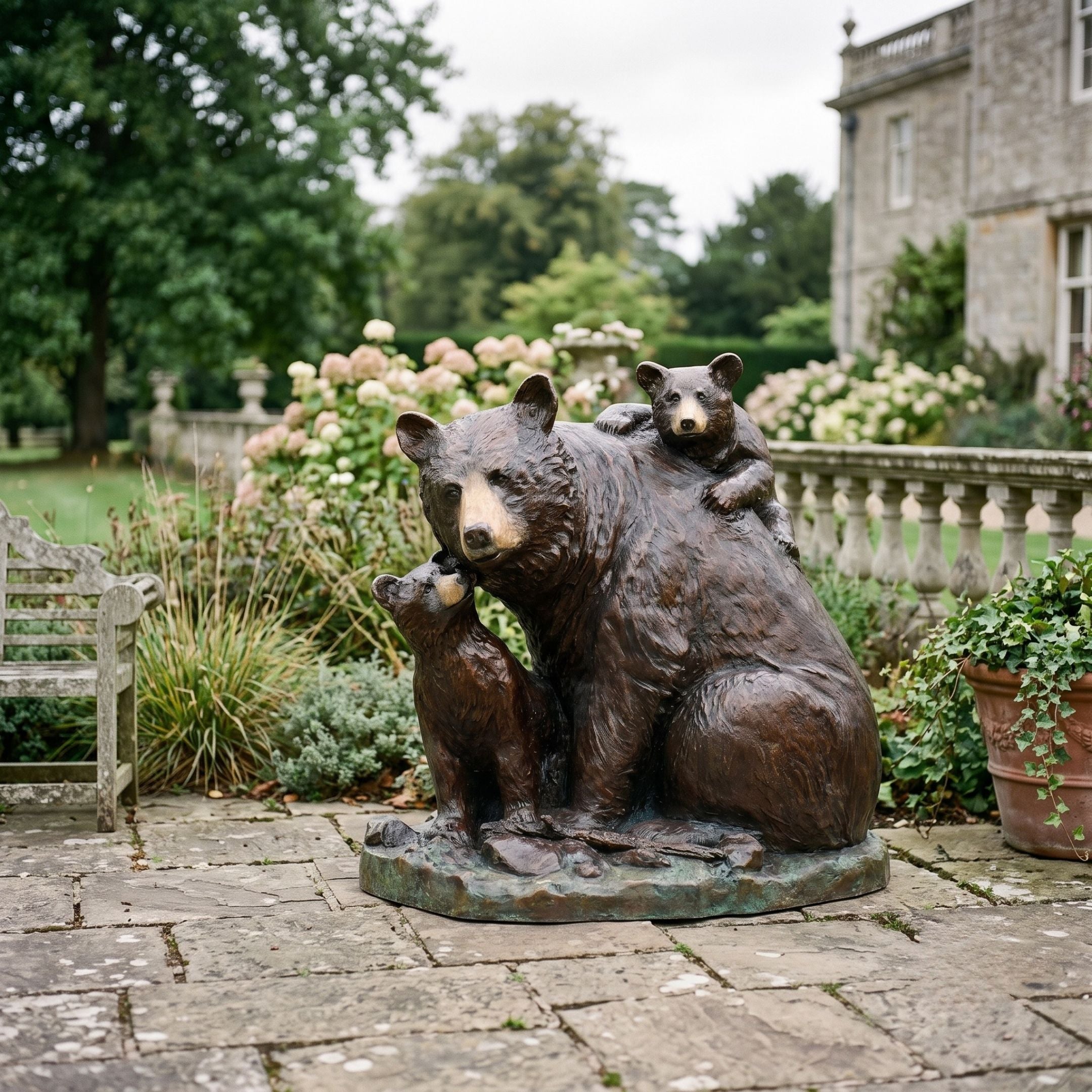 Large Traditional Mother Bear and Cubs Bronze Sculpture by Giant Sculptures on a garden patio, one cub nuzzling her muzzle and another draped across her back.