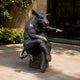 Life-Size Contemporary Wild Boar on Bench Bronze Sculpture by Giant Sculptures, seated on a cylindrical base with dark patina and golden accents in a sunlit courtyard.