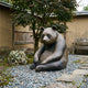 Life-Size Contemporary Seated Panda Bronze Sculpture by Giant Sculptures on pebbles beside a mossy rock and Japanese maple in a walled garden courtyard.