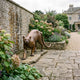 Life-Size Traditional Stalking Cougar Bronze Sculpture by Giant Sculptures in warm golden-brown patina, positioned on a stone garden path beside hydrangeas and a manor house.