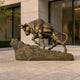 Monumental Traditional Straining Bull Bronze Sculpture by Giant Sculptures, 230cm, shown hauling a strapped pack on a rocky base outside a stone-clad building.