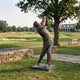Giant Sculptures Contemporary Life-Size Male Golfer Bronze Sculpture 230cm in follow-through pose on a low plinth beside a stone wall on a golf course.