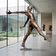Giant Sculptures' 260cm Large Contemporary Leaping Male Figure Bronze Sculpture with warm patina, shown mid-leap on a small base in a light gallery beside glass.
