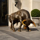Large Contemporary Charging Bull Bronze Sculpture by Giant Sculptures with dark brown patina and golden horns, head lowered, displayed outside a stone building entrance.