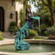 Classical Mermaid Fountain Bronze Sculpture by Giant Sculptures with dual-tone patina, pouring water from a shell dish into a garden pool by a stone manor.