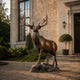 Life-Size Alert Bull Elk Bronze Sculpture by Giant Sculptures on a rocky base, standing on gravel outside a stone manor entrance with topiary and tall windows.