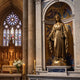 Life-Size Classical Virgin Mary Bronze Statue by Giant Sculptures displayed in a cathedral niche with gold mosaic, marble surround, candles, and stained glass beyond.