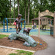 Traditional Boy and Dog Bronze Sculpture by Giant Sculptures displayed at Sunny Acres Playground, boy mid-stride on a verdigris log with a small dog beside him.