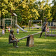 Life-Size Contemporary Children on Seesaw Bronze Sculpture by Giant Sculptures, dark patina finish, installed on a grassy playground with slide and swings.