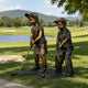 Life-Size Children Playing Golf Bronze Sculpture by Giant Sculptures showing a girl and boy in caps mid-putt on a grassy lawn beside a golf course pond.