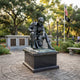 Life-Size Traditional Seated Soldier Bronze Sculpture by Giant Sculptures on a granite plinth in a memorial garden with American flag and plaques behind.