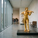 Monumental Classical Violinist Bronze Sculpture by Giant Sculptures, gold-gilt figure mid-performance on a black plinth in a bright gallery interior.