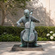 Life-Size Contemporary Seated Cellist Bronze Sculpture by Giant Sculptures with verdigris patina, shown on a stone plinth in a garden with hydrangeas.