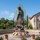 Monumental Traditional Our Lady of Guadalupe Bronze Statue 450cm by Giant Sculptures in polychrome finish with gold mandorla, displayed in a garden courtyard.