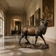 Life-Size Bugling Bull Elk Bronze Sculpture by Giant Sculptures displayed in a grand hallway with tapestries and paintings, head raised mid-call on a rocky base.