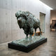 Life-Size Traditional Bison Bronze Sculpture by Giant Sculptures with green verdigris patina, displayed on a low black plinth in a concrete-walled gallery.