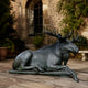 Monumental Reclining Moose Bronze Sculpture by Giant Sculptures with green-black patina, resting on stone paving before an arched window in a courtyard.