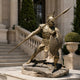 Life-Size Classical Ancient Warrior Bronze Statue by Giant Sculptures in polished gold finish, lunging with spear and shield on a stone base outside a columned building.