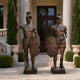 Life-Size Classical Roman Soldier Pair Bronze Sculpture by Giant Sculptures, 210cm warriors with shields and spear on plinths, flanking a columned entrance.
