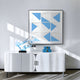 A modern interior features a white sideboard topped with a translucent blue glass sculpture and two small blue boxes. Above it hangs the Giant Sculptures Prismatics Blue Geometric Cardboard Carving Wall Art, creating a sophisticated look with its blue and white shapes.