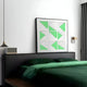 A modern bedroom showcases a dark green bedspread and pillows. Above the bed, the captivating Prismatics Green Geometric Cardboard Carving Wall Art by Giant Sculptures adds charm. A small pendant light, a bedside lamp, and a gray curtain partially covering the window enhance the ambiance.