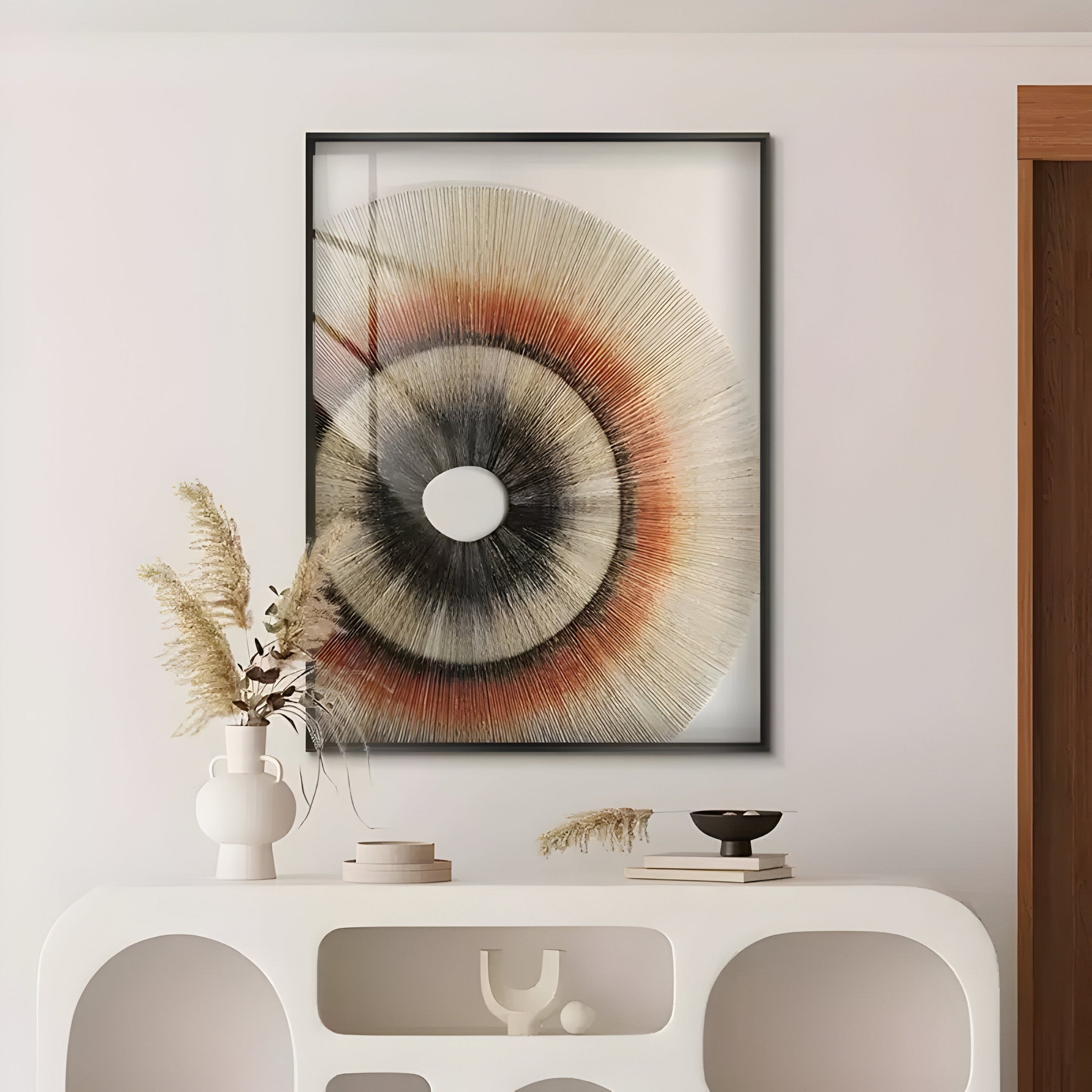 A modern living room features the Giant Sculptures Auralis Earthy Tone Concentric Circular Cardboard Craft Wall Art. A white console below holds vases, dried plants, and a small bowl, while the warmth of a wooden door frame complements this contemporary display.