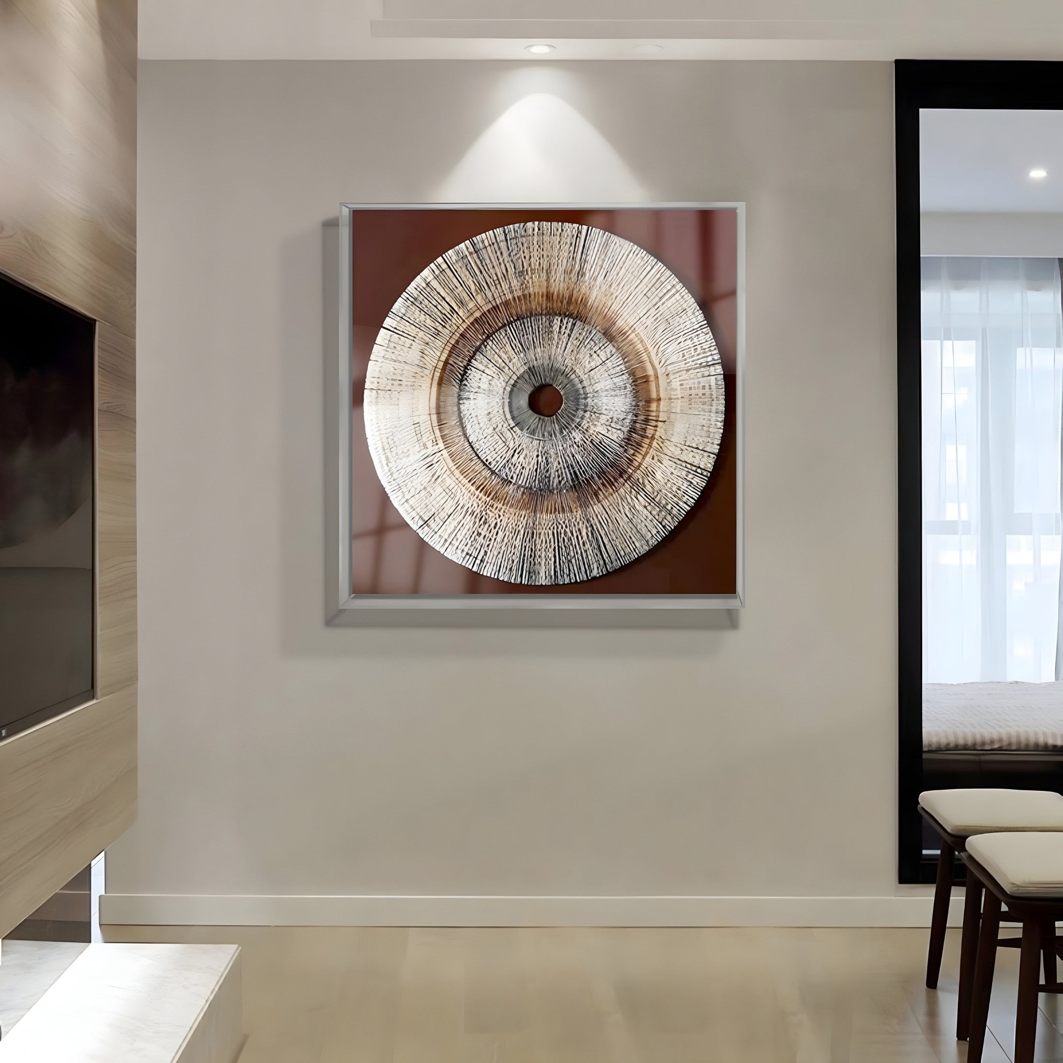 A modern living room showcases the Oculis Rustic Warmth Square Handmade 3D Paper Wall Art by Giant Sculptures. Featuring concentric textured rings in earthy brown and beige hues, it adds rustic warmth above a light wood floor with a black-framed mirror and sheer-curtained window.