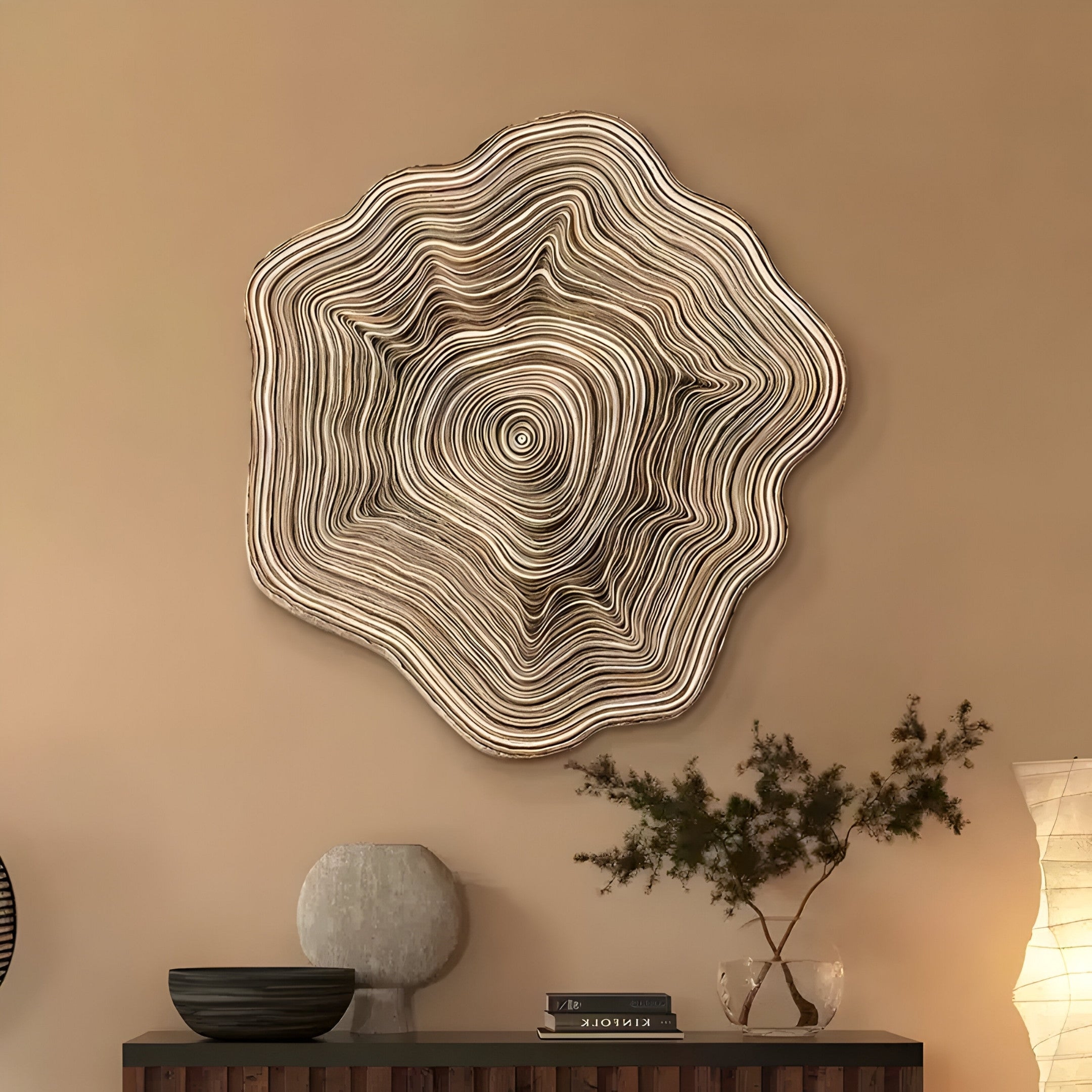 The Lignature Ring Hand-Painted Felt Paper Wall Art by Giant Sculptures, featuring a tree ring motif and layered design, hangs on a beige wall. Below, a Japanese retro wooden sideboard holds two books, a globe-shaped vase, a small plant, and a glowing lamp.