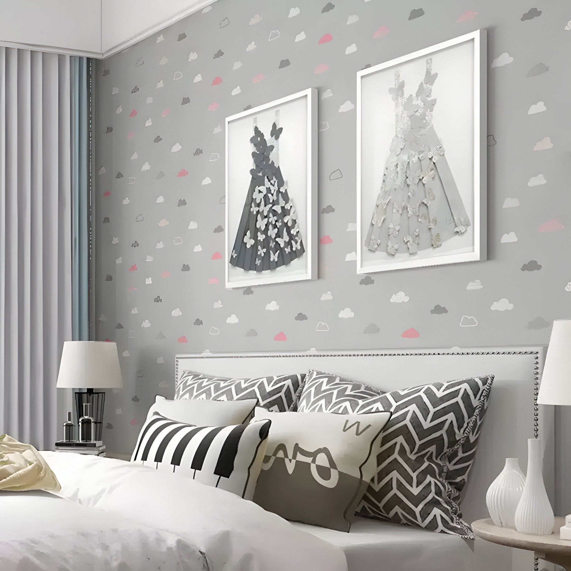 A modern bedroom has a bed with patterned pillows and a cushioned headboard. The wall showcases Giant Sculptures Flutter Grey & White Butterfly Dress 3D Wall Art against gray cloud-patterned wallpaper. A table lamp sits on the nightstand near a tall window with vertical blinds.