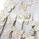 The Flutter Grey & White Butterfly Dress 3D Wall Art by Giant Sculptures showcases handmade butterfly-shaped cutouts from printed text paper, arranged in a scattered pattern on a light gray surface for a textured, stunning effect.