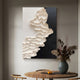 The Stratura II Black & White Layered Paper Canvas Wall Art by Giant Sculptures exhibits monochrome artistry with textured white forms on the left and a smooth black backdrop on the right. It hangs elegantly above a round wooden table decorated with a vase of dried flowers and two oranges.