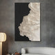 The Stratura V Black & White Layered Paper Canvas Wall Art by Giant Sculptures showcases abstract white wave-like textures on a black background, enhancing the stylish, contemporary room setting with a minimalist lamp and couch nearby.