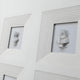 The Lustella White Plaster Statue Square Cardboard Wall Art by Giant Sculptures features two elegant white plaster busts mounted side-by-side in layered square frames on a white wall, creating recessed niches that cast subtle shadows to enhance their classical allure.